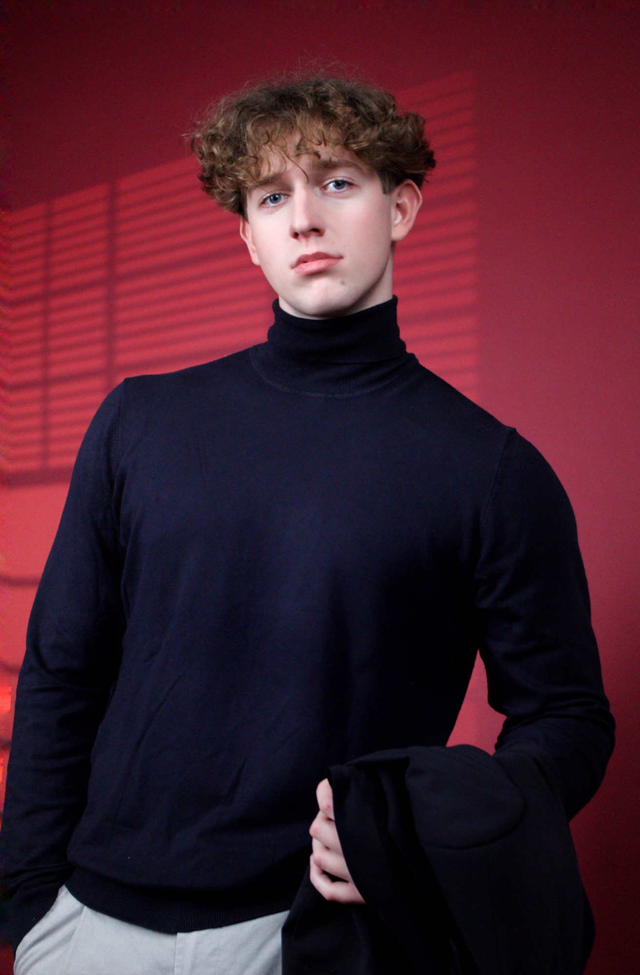Studio portrait of a young man in a navy turtleneck against a red wall